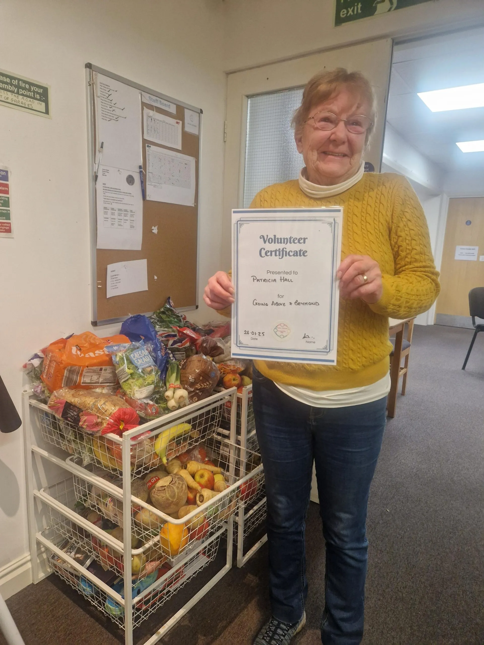 A Colne Citadel volunteer holding her volunteer certificate next to food donations